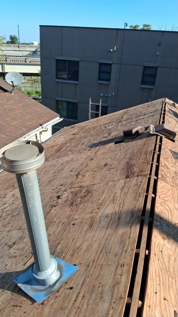 Weathered plywood roof sheathing and old ventilation components before a Jersey City reroof
